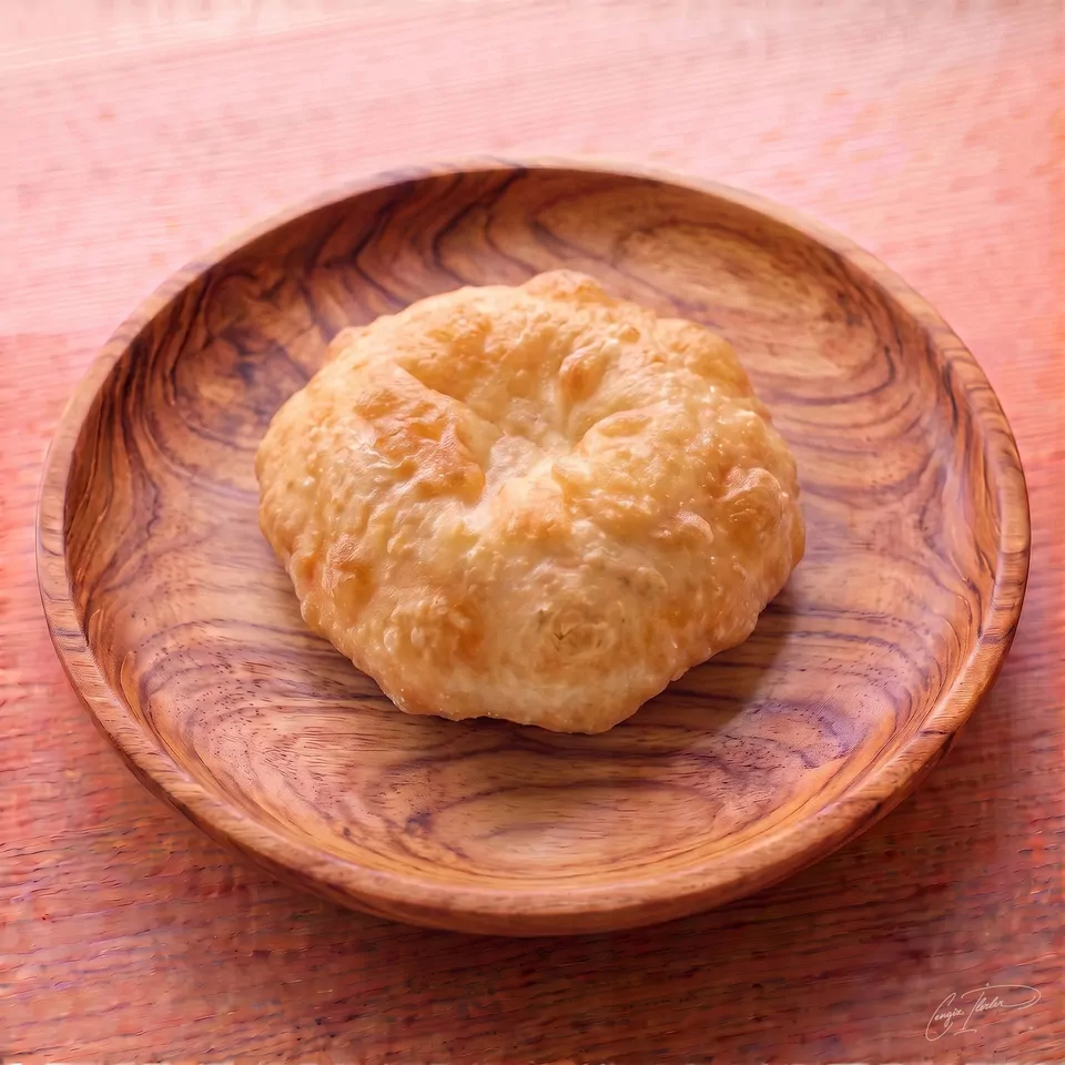 A single piece of golden, puffy pişi — Turkish fried dough — on a carved wooden plate.