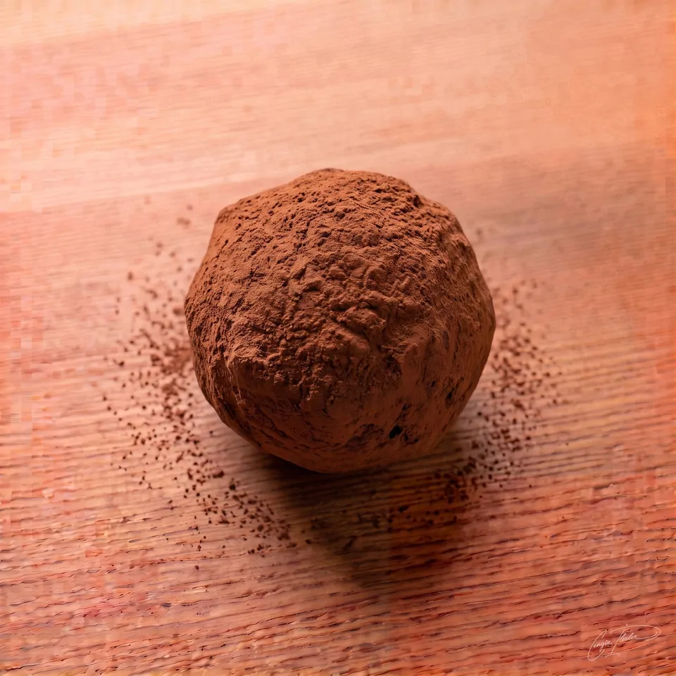A round cocoa-dusted chocolate truffle on a white plate on a wooden table.
