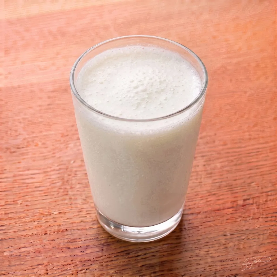 A tall glass of frothy ayran — the salted yogurt drink — with a foamy white top.