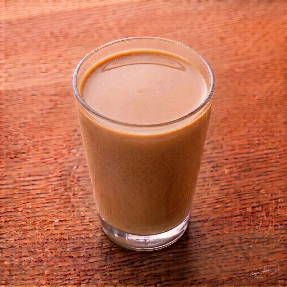 A cold glass of milk mixed with carob molasses, giving it a creamy light brown color, with condensation on the outside of the glass.