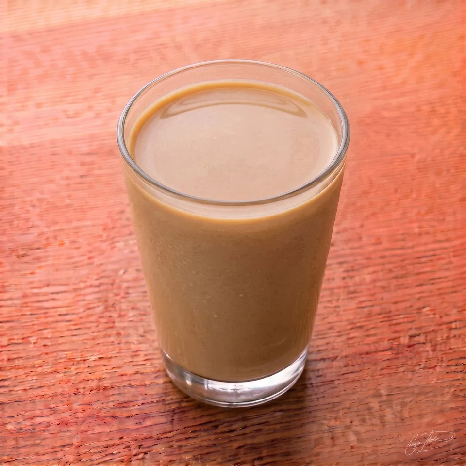A glass of creamy, light brown milk coffee resting on a wooden surface.