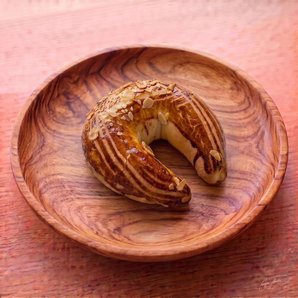 A classic crescent-shaped Turkish ay çöreği on a carved wooden plate, topped with a rich dark glaze and sliced almonds.