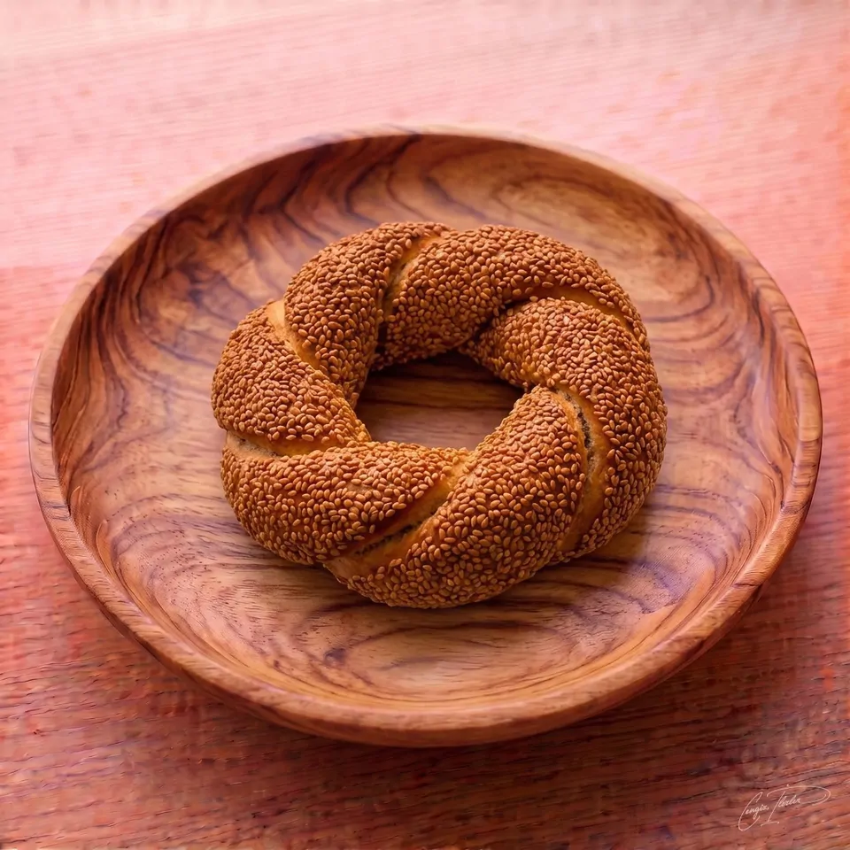 A single large, round Turkish simit — a twisted, circular bread heavily encrusted with toasted sesame seeds — resting on a carved wooden plate.