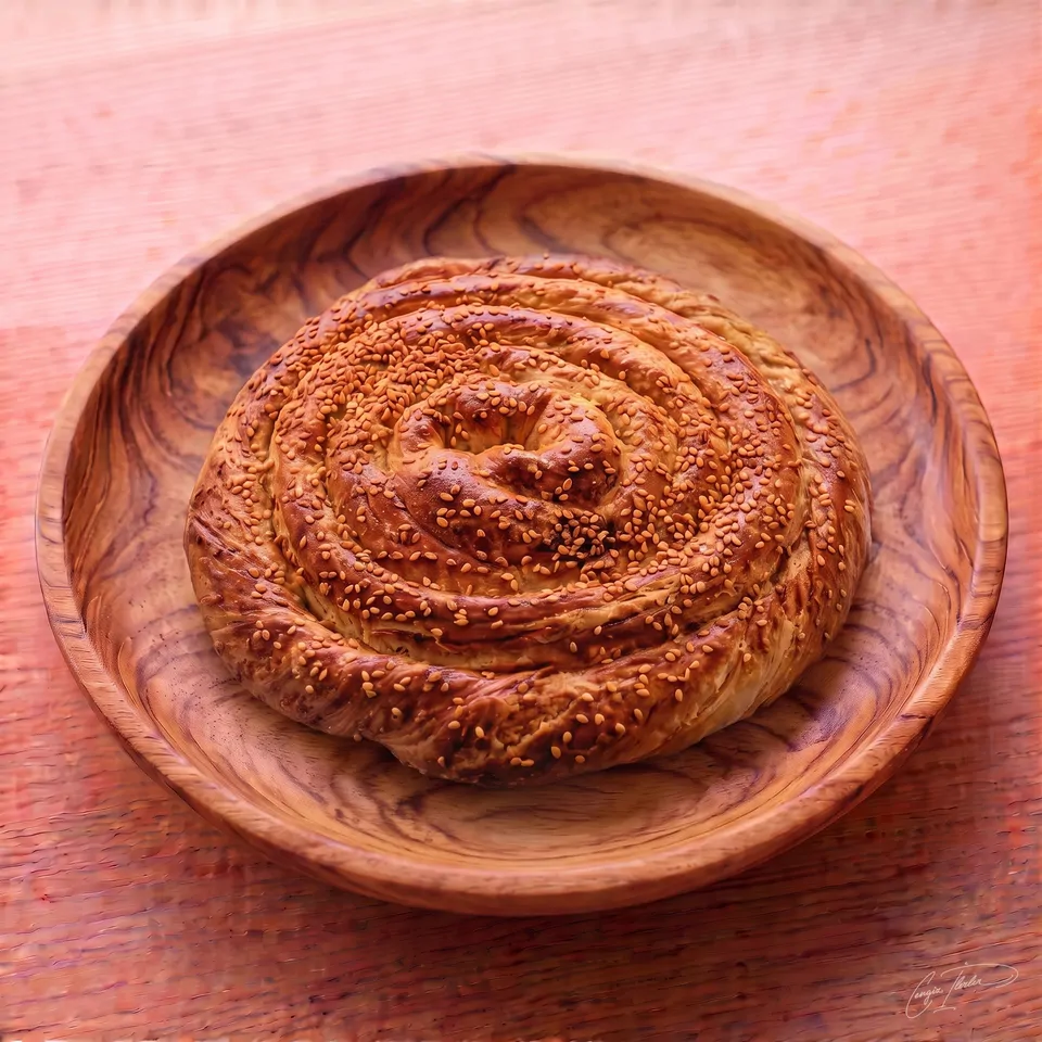 A large, round, spiraled tahinli çörek with a glossy, golden-brown crust generously sprinkled with sesame seeds, resting on a carved wooden plate.