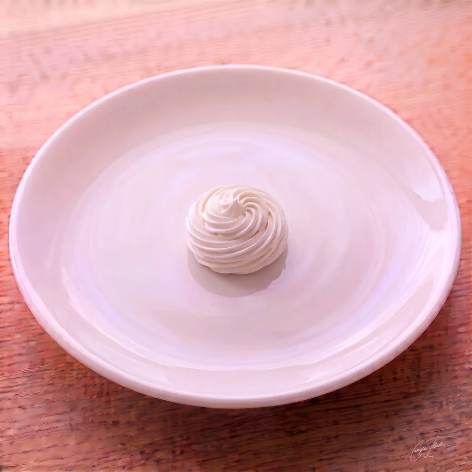 A single white meringue piped into a tall swirled spiral dome, on a white plate on a wooden table.